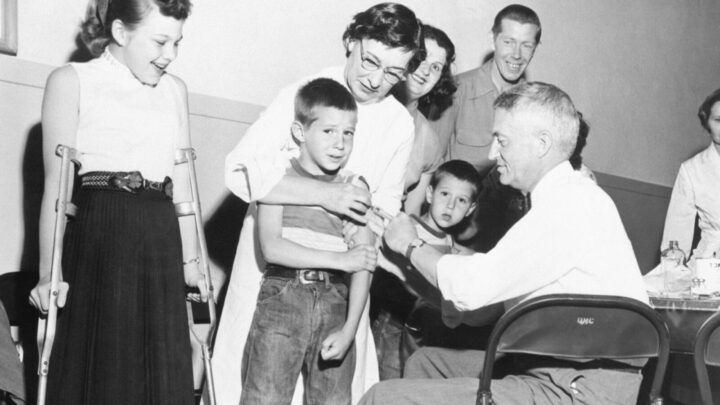 Doctor giving a shot of the Salk anti-polio vaccine to a boy, 6, while the boy's sister, 12, a polio victim, looks on, in April 1955. Source: Getty