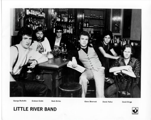 Black-and-white promotional photo of six band members seated around a bar, with bottles and glasses behind them.