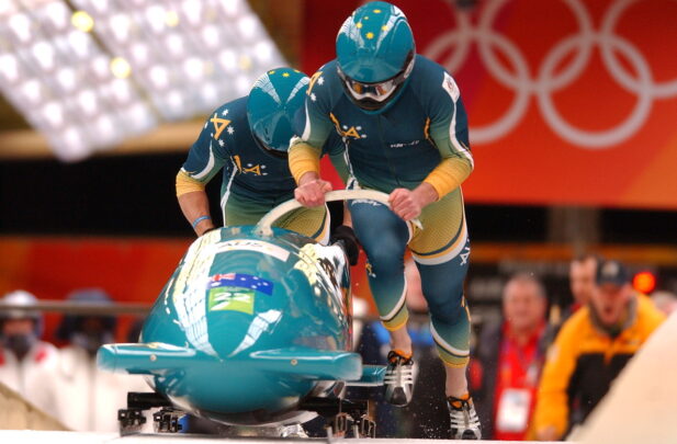 Two Australian bobsled athletes push their sled at the start of an Olympic race.