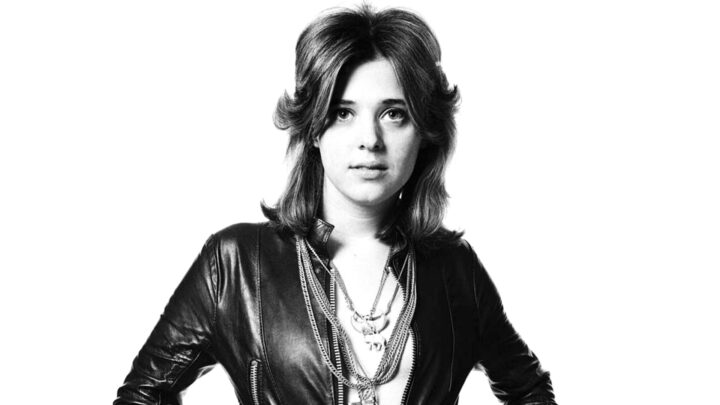 Black-and-white portrait of a young Suzi Quatro wearing a leather jacket and layered necklaces.
