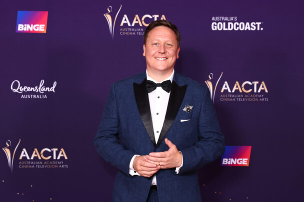 Man in a tuxedo posing on an awards event red carpet.